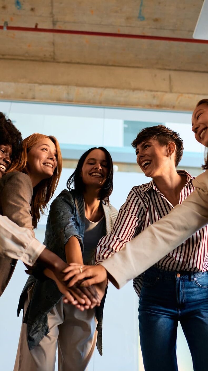 Women standing in a circle with their hands stacked in the middle during a team huddle, symbolizing leadership and support.